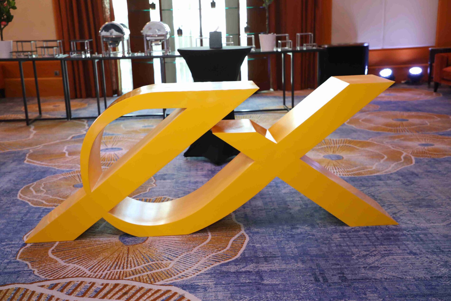 Forex Traders Summit Dubai 2023: Large yellow Exness logo displayed in the exhibition area with buffet tables in the background.