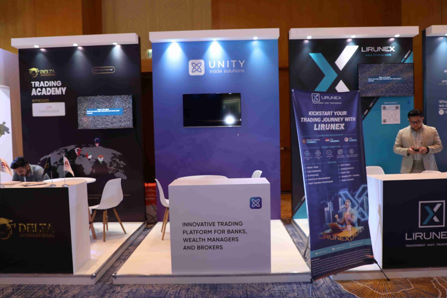 Booths at the Forex Traders Summits Dubai 2023,featuring Delta International, Unity Trade Solutions, and Lirunex. The Delta International booth promotes their Trading Academy. Unity Trade Solutions' booth highlights their innovative trading platform for banks, wealth managers, and brokers. The Lirunex booth encourages visitors to 'kickstart your trading journey with Lirunex' and emphasizes their transparent, safe, and trustworthy services.